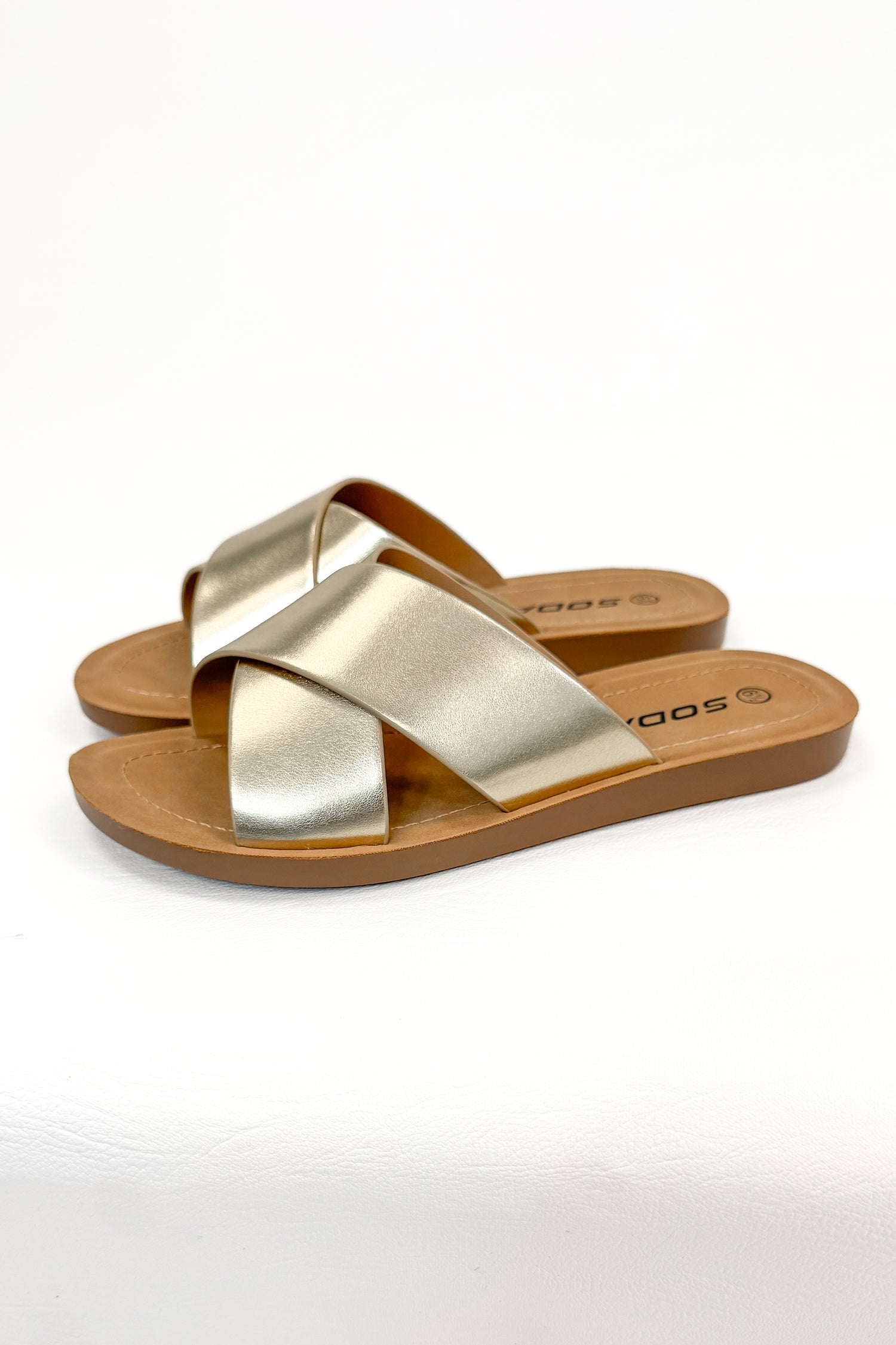Reflect- Gold Cross Strap Sandals against white studio background side view.