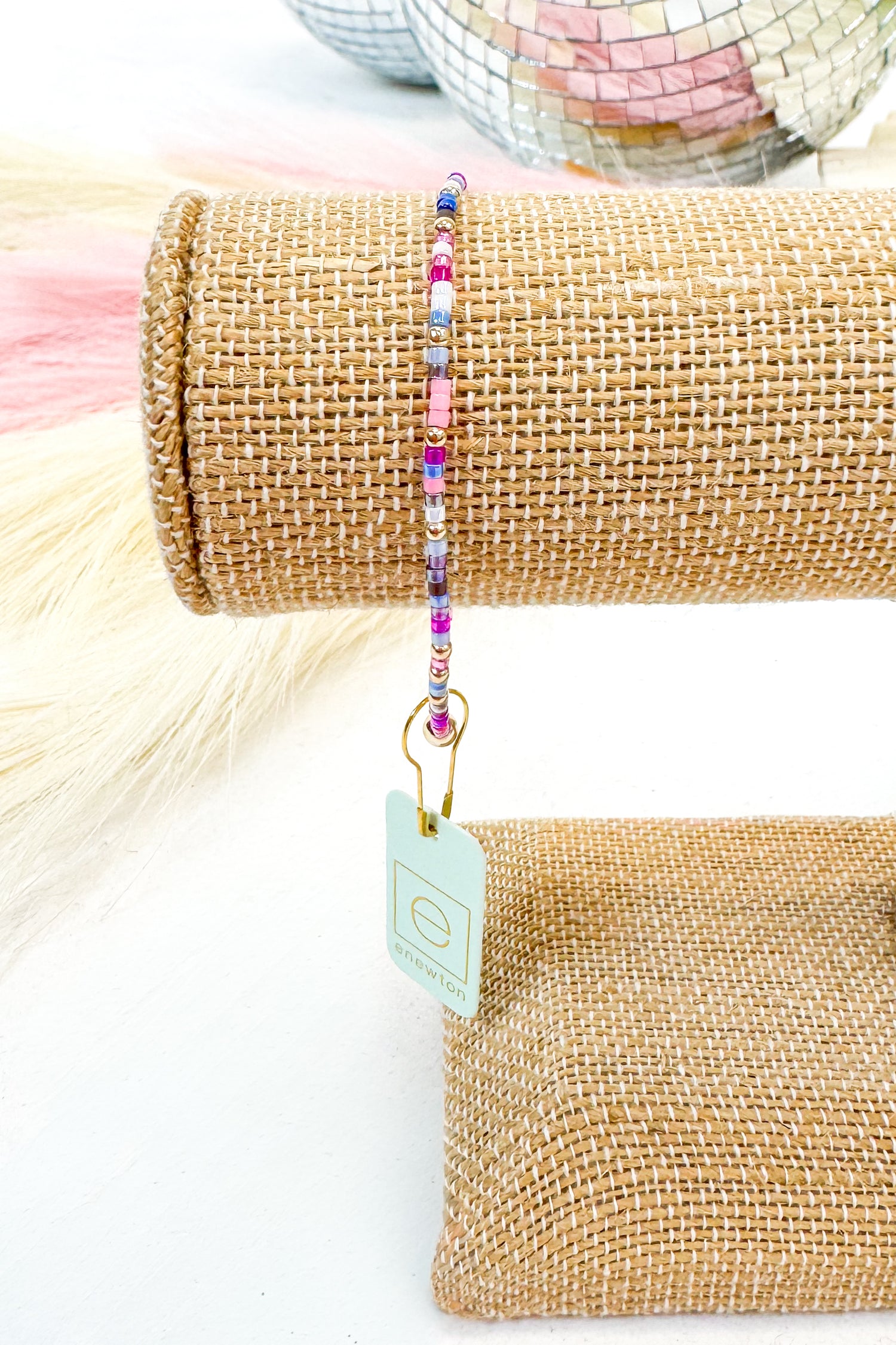 Roll of burlap with a colorful beaded bracelet on top, against a neutral background.