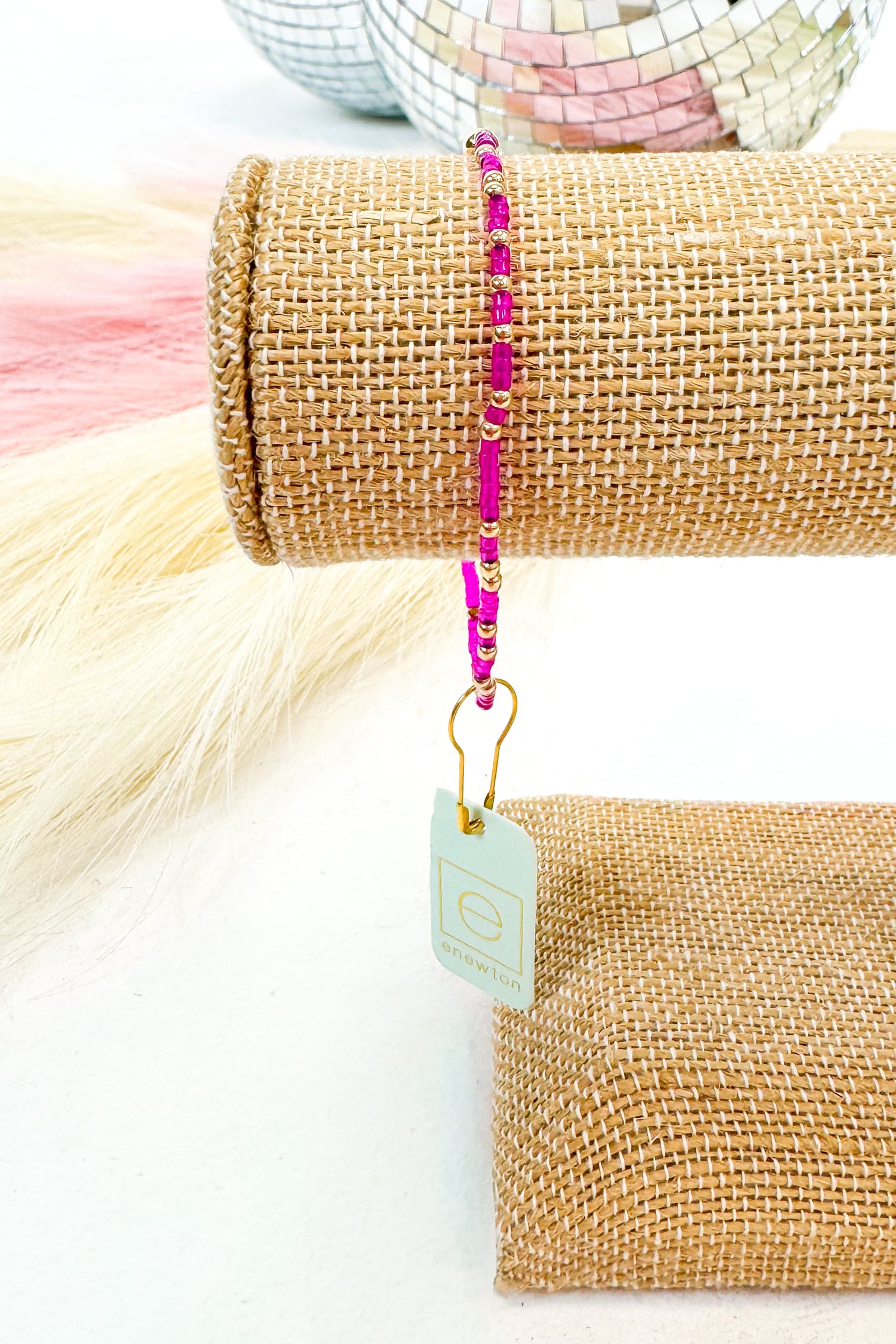 Pink beaded bracelet on a roll of burlap with a tag, against a white background