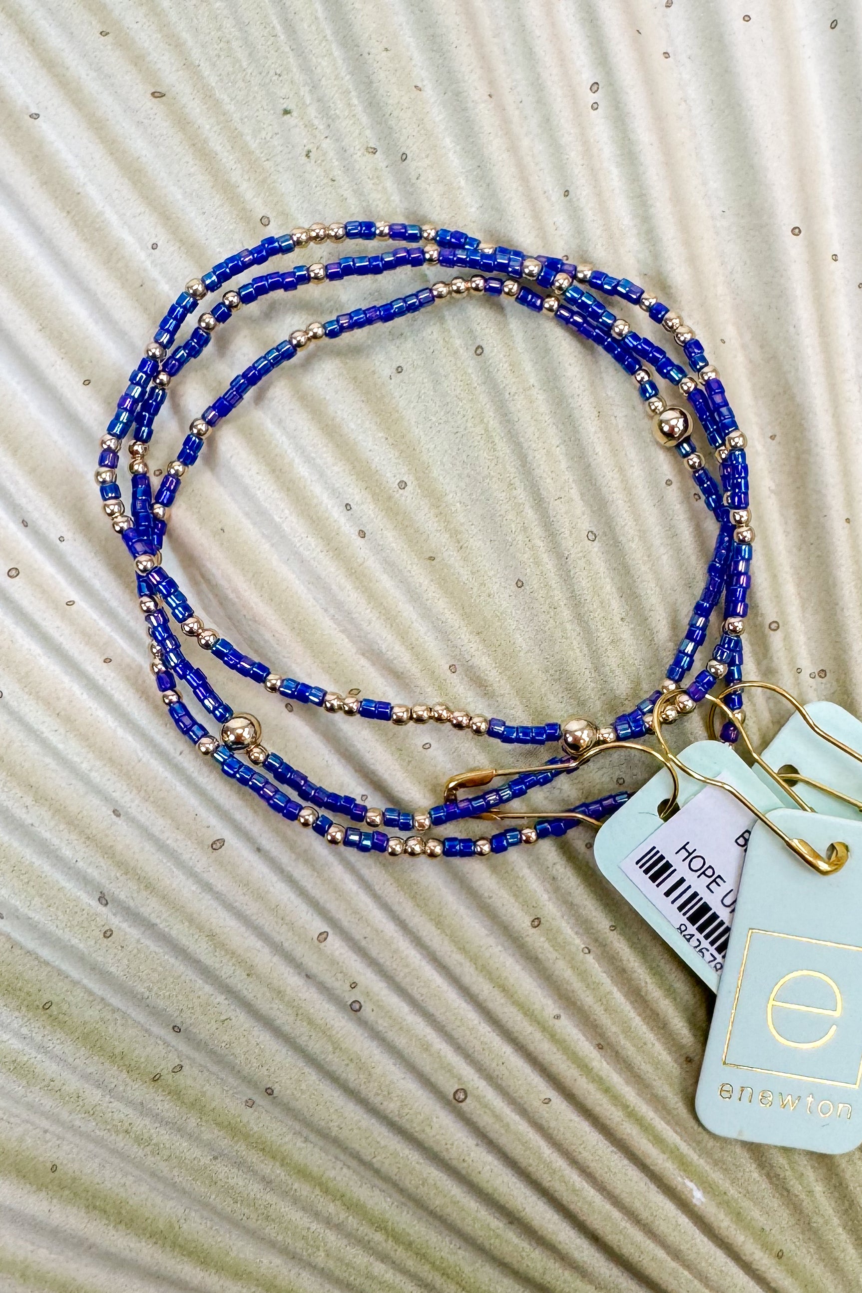 Blue beaded bracelets with gold accents on a textured beige surface