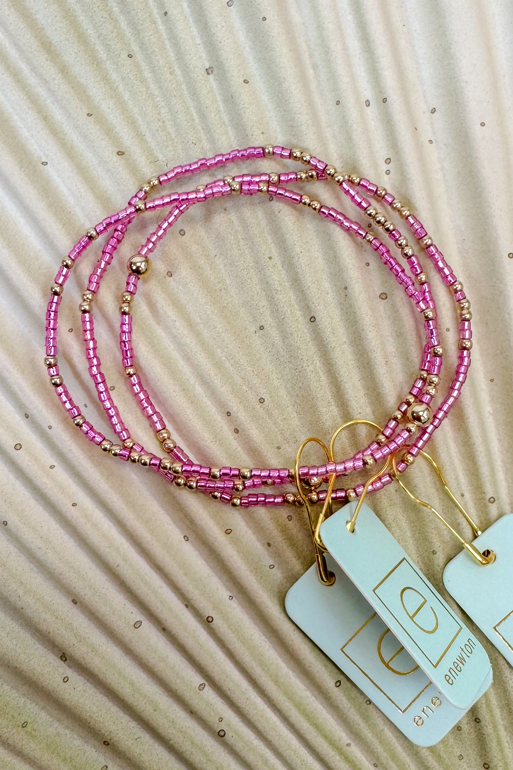 Pink beaded bracelets with gold accents on a textured beige surface