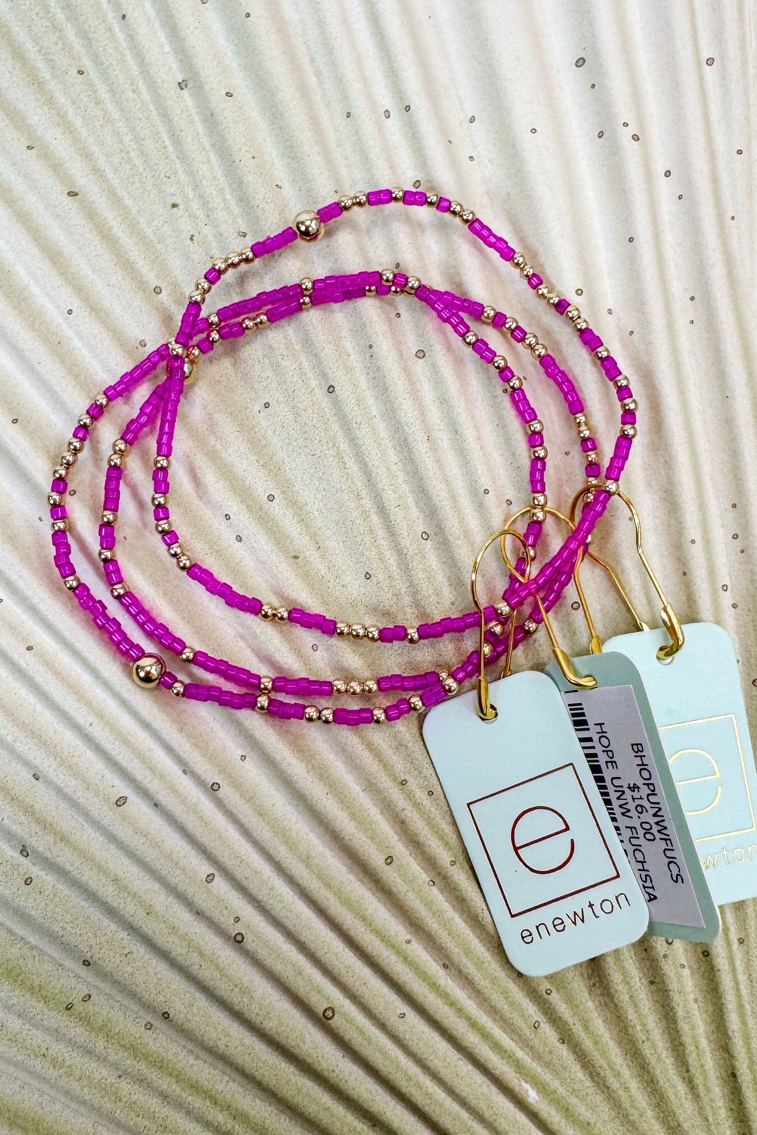 Set of pink beaded bracelets with gold accents on a textured beige surface, featuring &