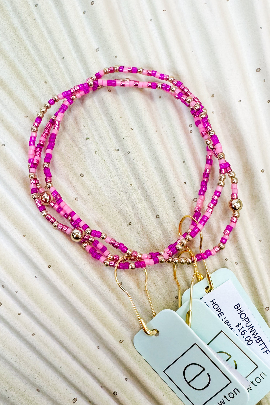 Pink beaded lanyard with gold accents on a textured beige surface