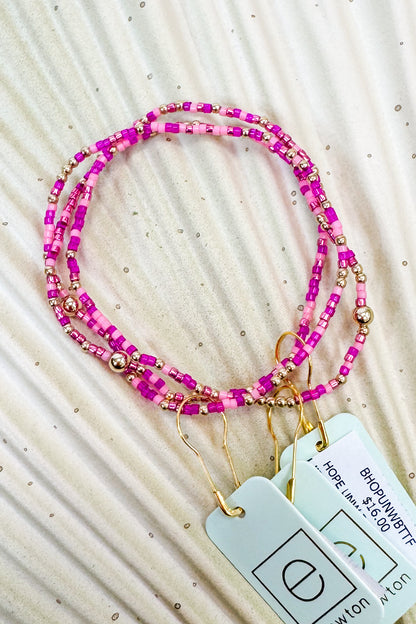 Pink beaded lanyard with gold accents on a textured beige surface