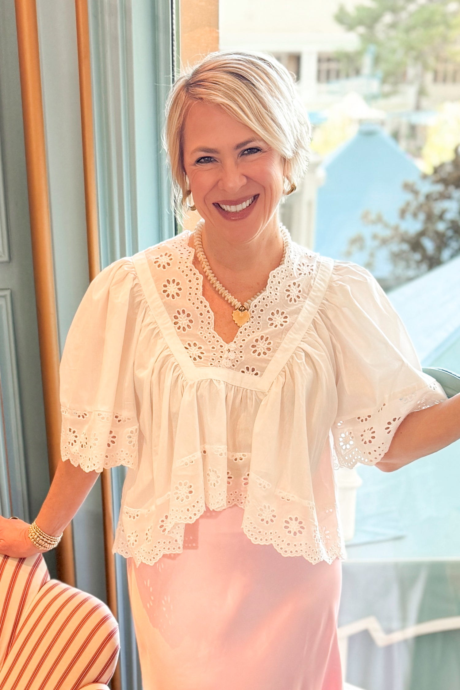 Woman wearing a white lace top and pink skirt indoors.