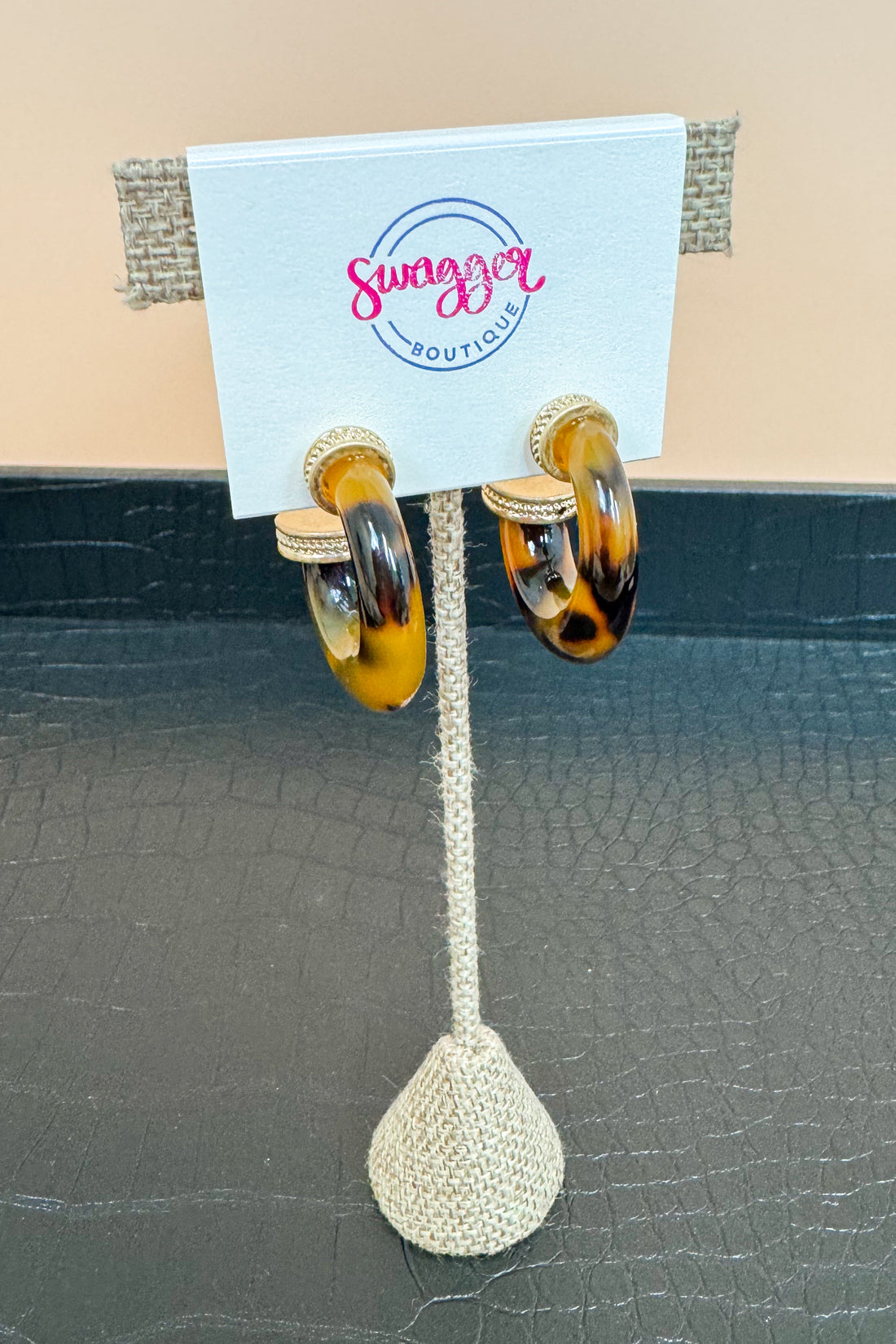 Pair of tortoiseshell hoop earrings on a Swagget Boutique card against a beige background.