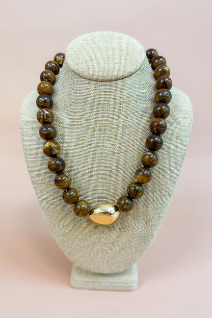 Beaded necklace with a gold clasp on a beige bust against a pink background