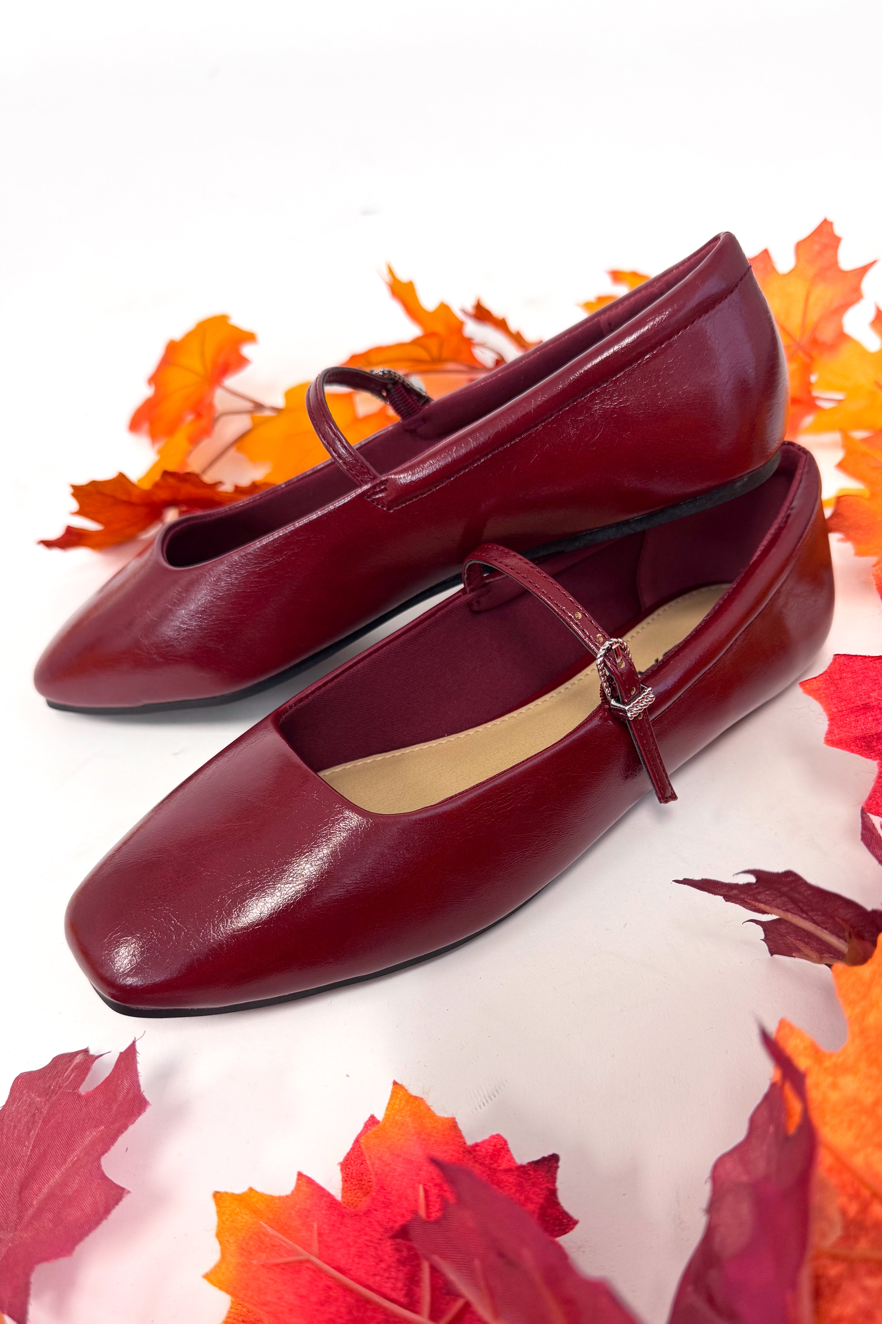 Pair of red shoes with a strap on a white background with autumn leaves.