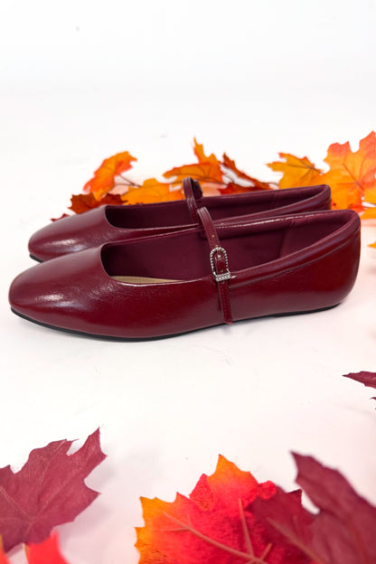 Red shoes with a strap on a white background with autumn leaves.