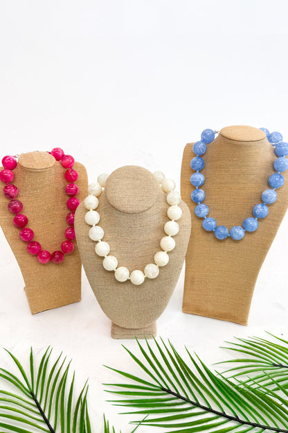 Three necklaces on mannequin heads with a white background and green leaves at the bottom.