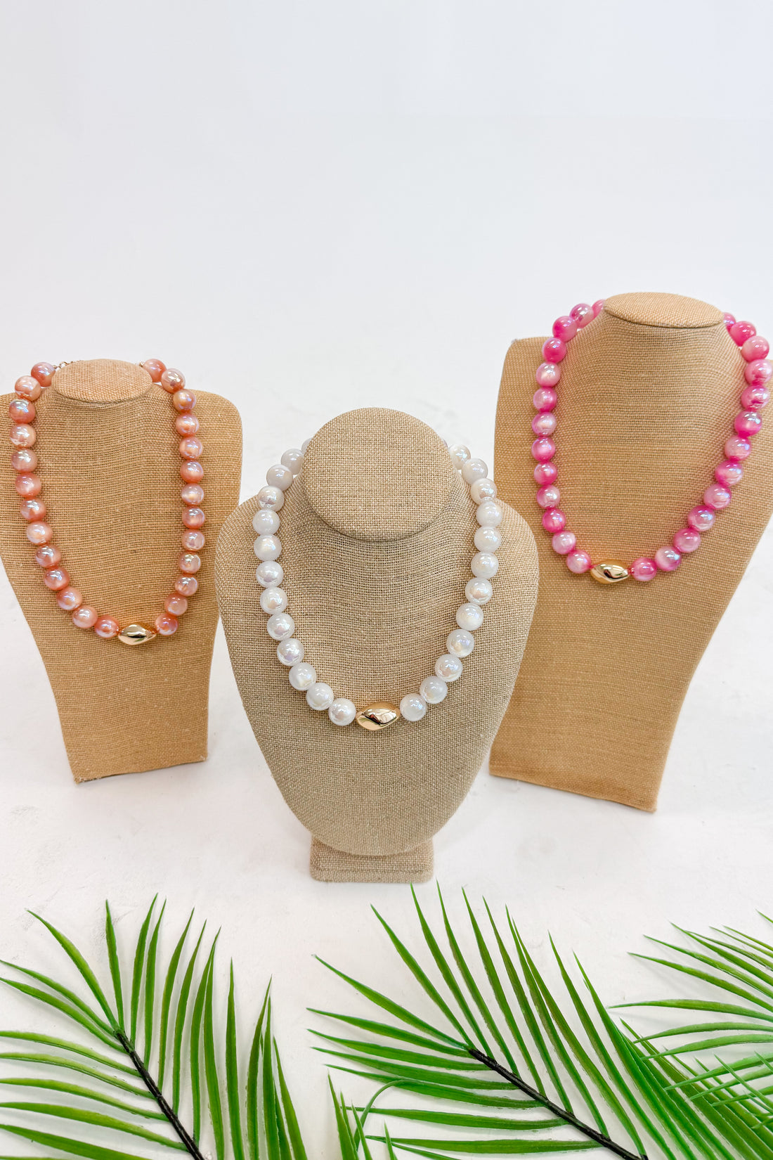 Three necklaces on mannequin heads with pink and white beads against a white background.
