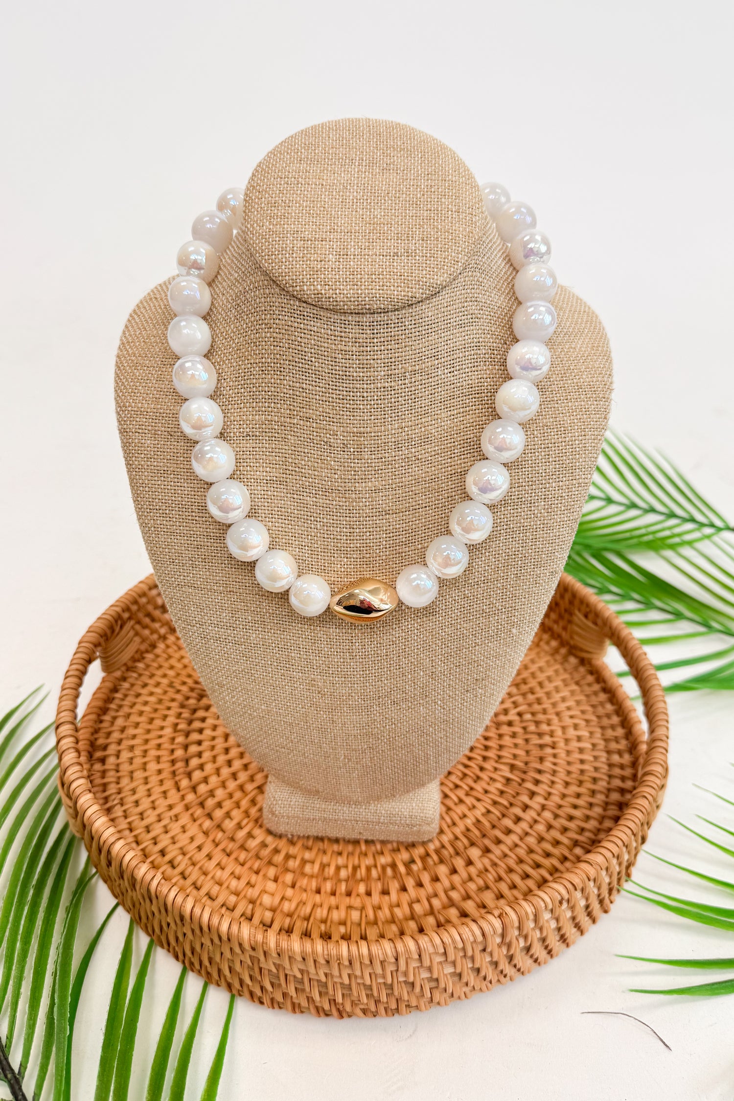 Pearl necklace on a beige bust with a woven base and green leaves in the background