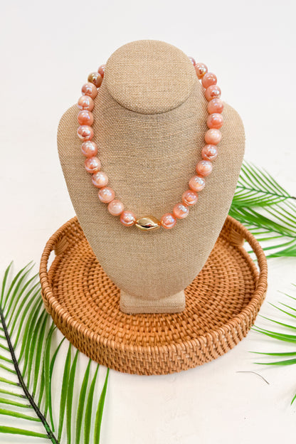 Necklace on a beige display bust with a woven base, surrounded by green leaves.
