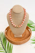Necklace on a beige display bust with a woven base, surrounded by green leaves.