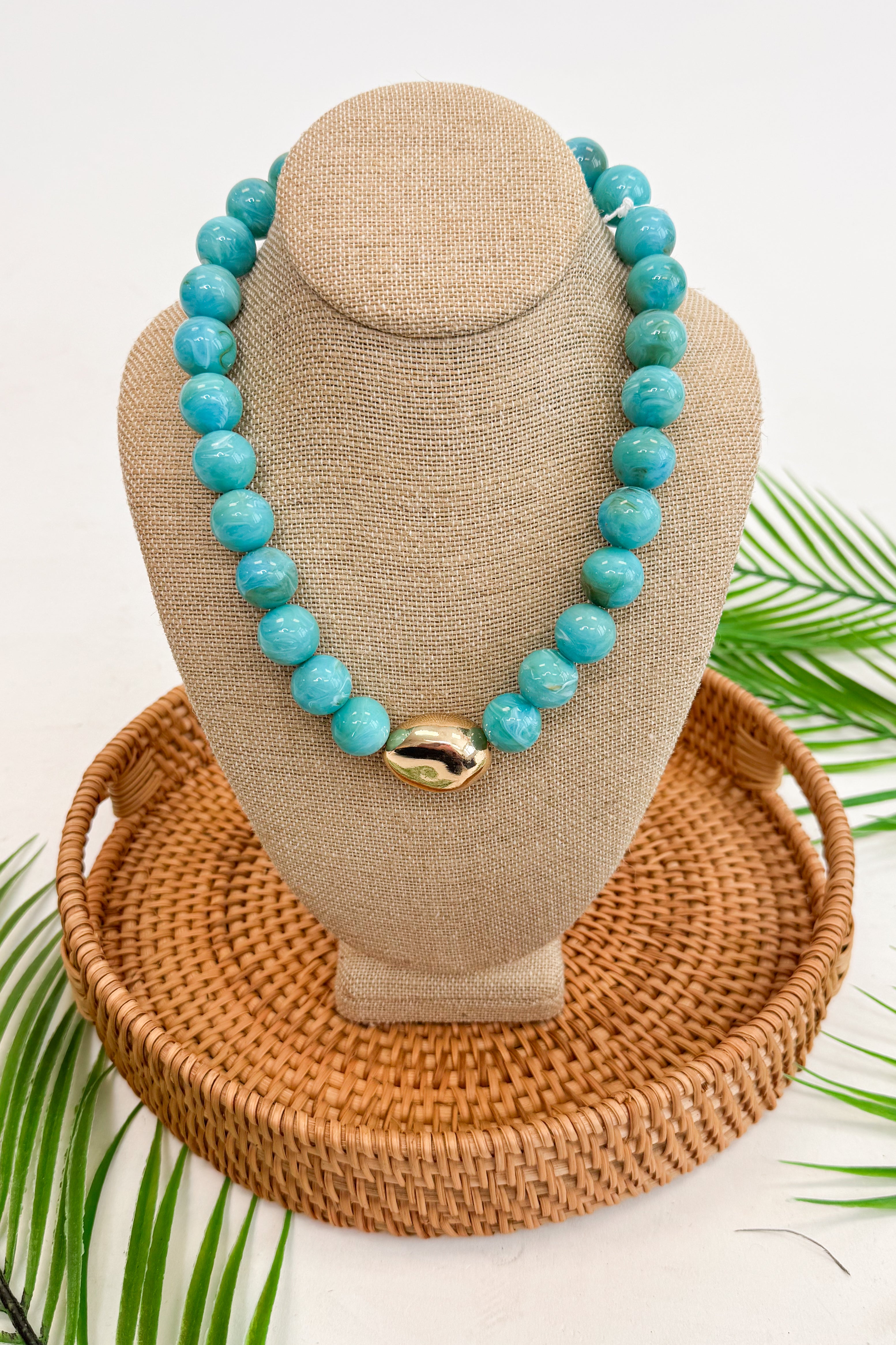Turquoise beaded necklace on a beige mannequin bust with a woven base.