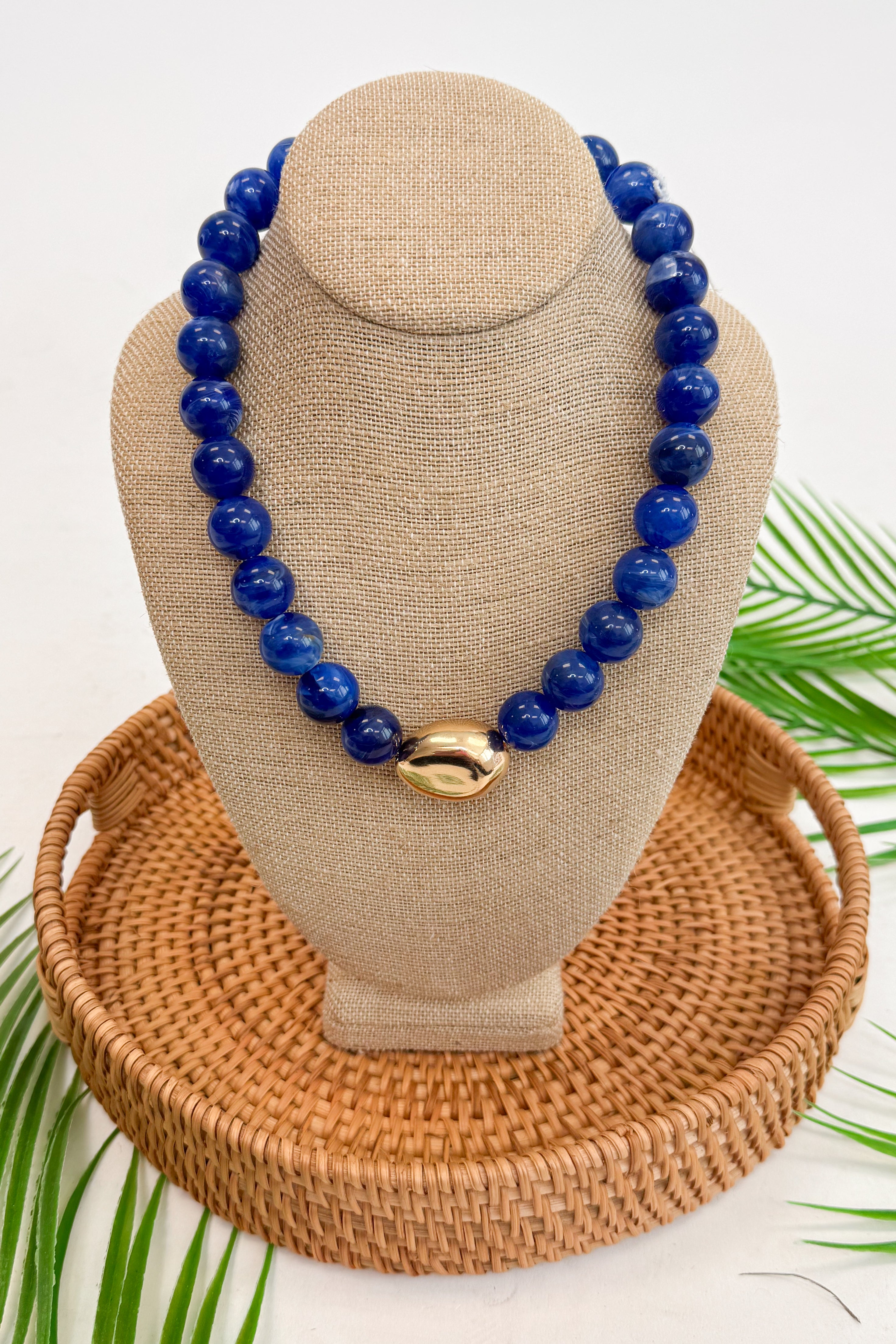 Dark blue beaded necklace on a beige mannequin bust with a woven base.