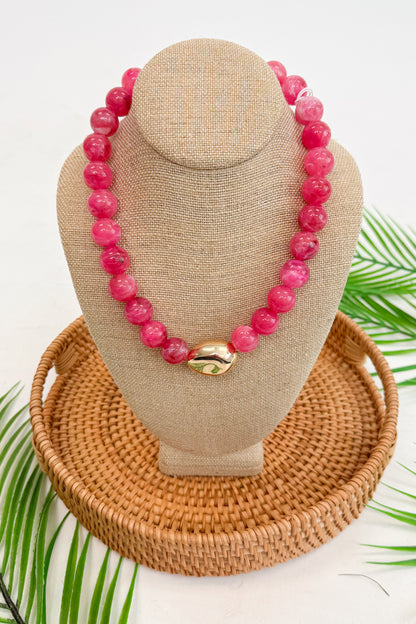 Pink beaded necklace on a beige bust with a woven base, surrounded by green leaves.
