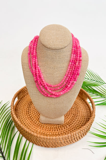 Neon pink beaded necklace on a mannequin bust with a woven basket and palm leaves in the background
