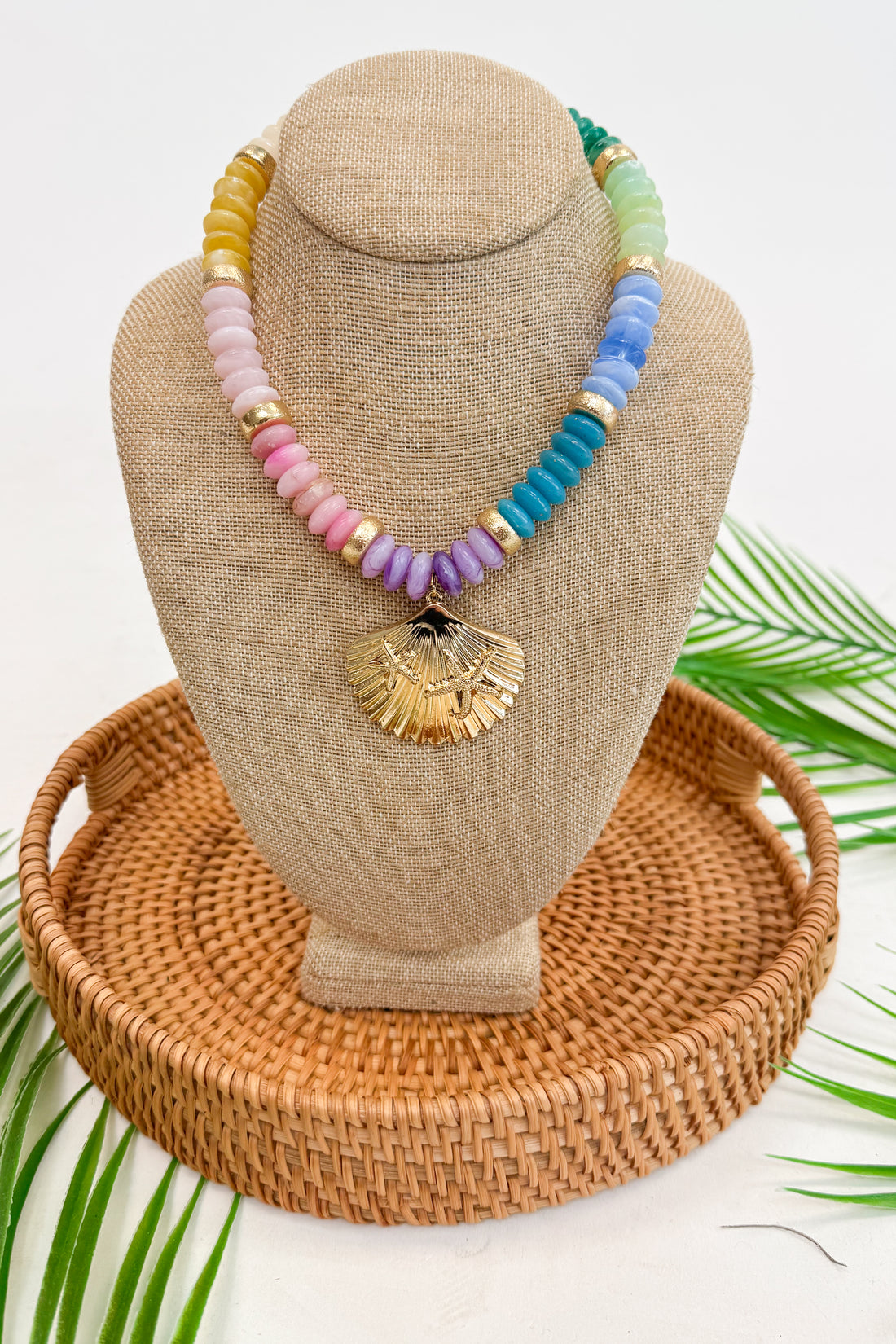 Colorful beaded necklace with a shell pendant on a tan bust with a woven base.