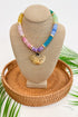 Colorful beaded necklace with a shell pendant on a tan bust with a woven base.