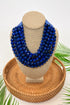 Blue beaded necklace on a mannequin bust with a woven basket and green leaves in the background