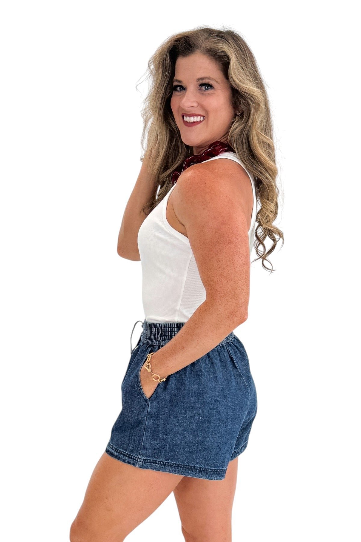 Side view of woman wearing Swagger Boutique’s Indigo Denim Shorts With Elastic Waist with top against white studio background.