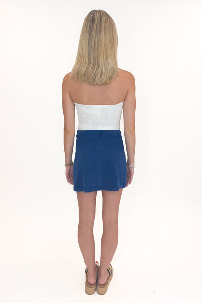 Back view of woman wearing Swagger Boutique’s Indigo Gail Jersey Denim Mini Skirt by Z Supply with white top against white studio background.
