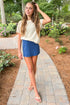 Front view of woman wearing Swagger Boutique’s Indigo Gail Jersey Denim Mini Skirt by Z Supply with Island Coconut Banyan Top by Z Supply walking down a walkway outside.