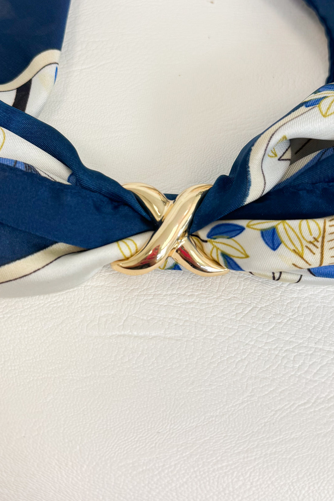 Gold-tone scarf ring enhancer securing a blue and white patterned scarf, shown styled at the center of the scarf on a white studio background