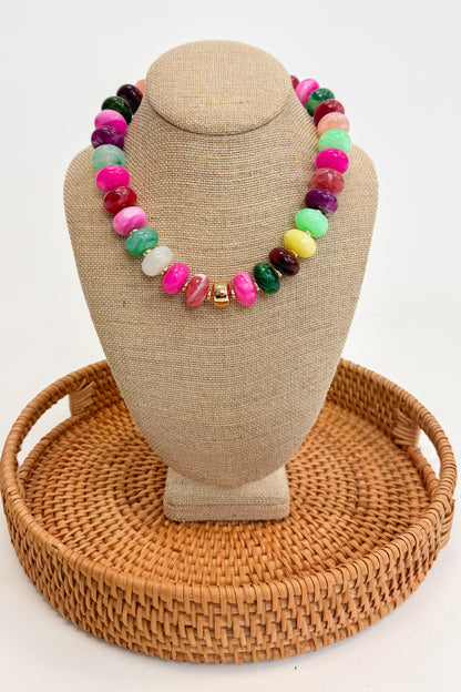 Colorful beaded necklace on a beige jewelry display with a woven base.