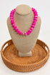 Necklace with pink beads on a beige mannequin bust with a woven brown base.