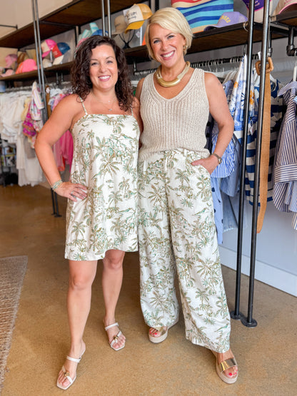 Front view of woman wearing Swagger Boutique’s Island Coconut Maude Tiki Tide Mini Dress by Z Supply with sandals and woman wearing coordinating pants and sweater at the store.