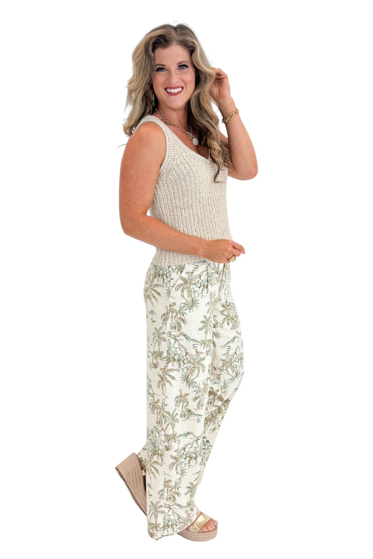 Side view of woman wearing Swagger Boutique’s Island Coconut Overlook Tiki Tide Linen Pants with Beige V-Neck Knitted Tank by Skies Are Blue against white studio background.