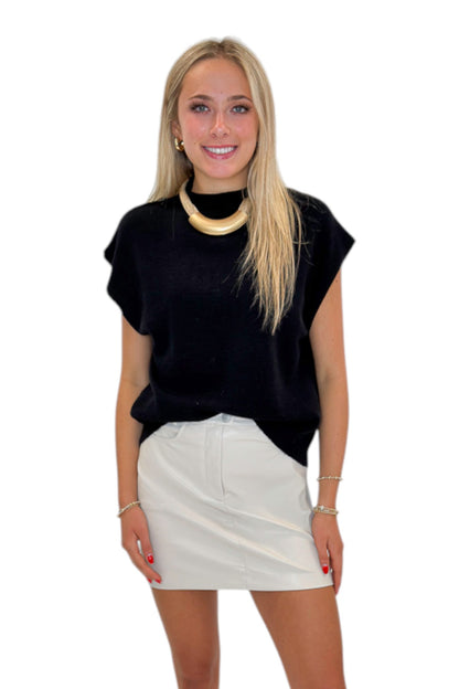Front view of woman wearing Swagger Boutique’s Ivory Faux Leather Mini Skirt with black sweater against white studio background.