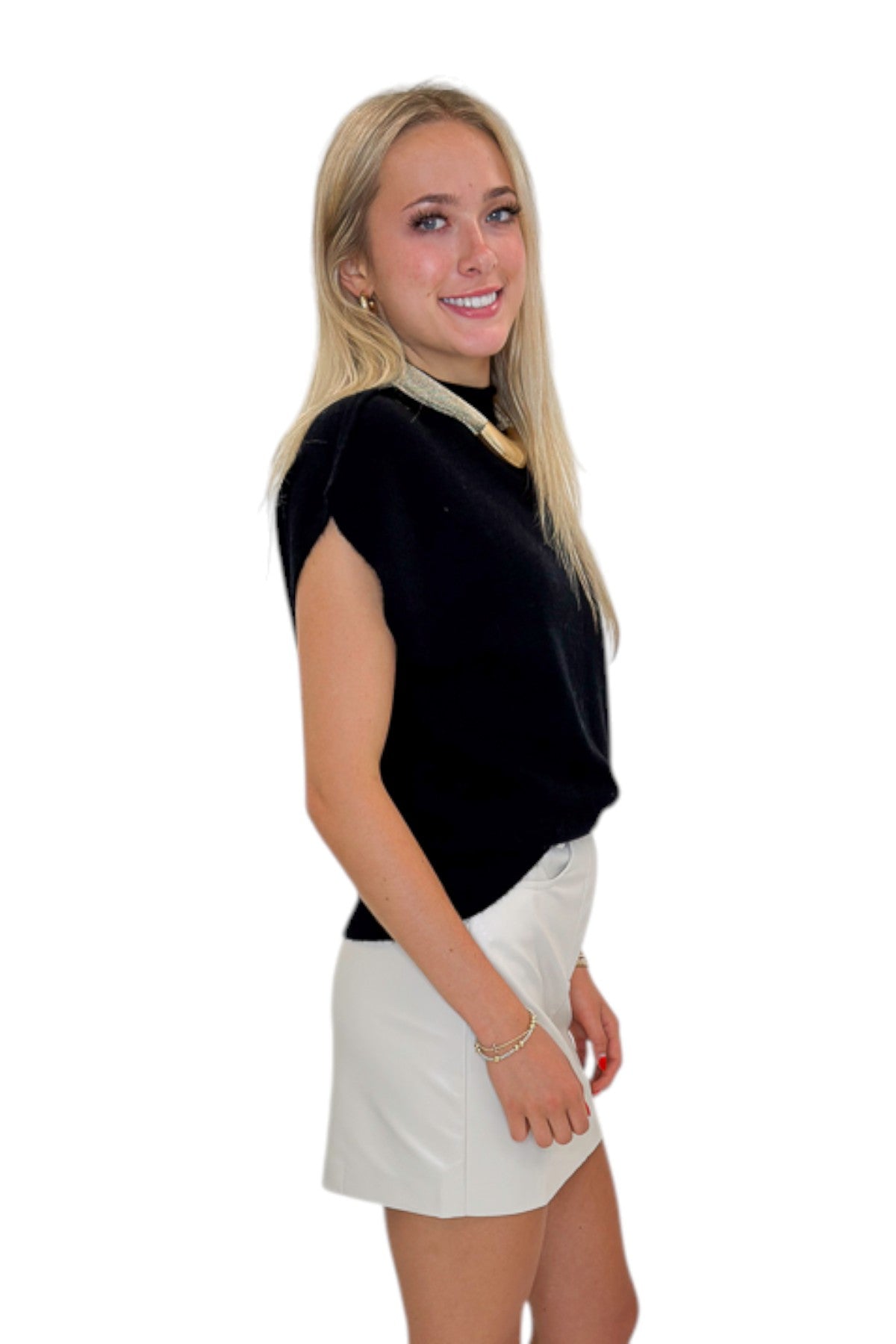 Side view of woman wearing Swagger Boutique’s Ivory Faux Leather Mini Skirt with black sweater against white studio background.