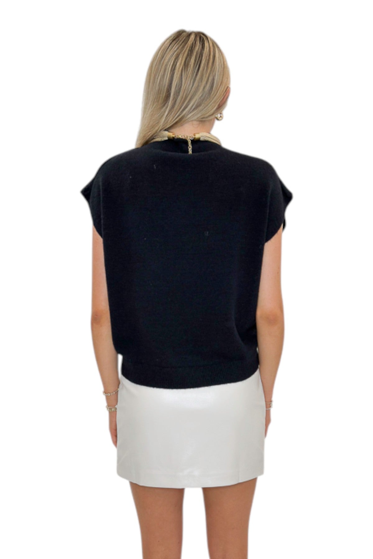 Back view of woman wearing Swagger Boutique’s Ivory Faux Leather Mini Skirt with black sweater against white studio background.