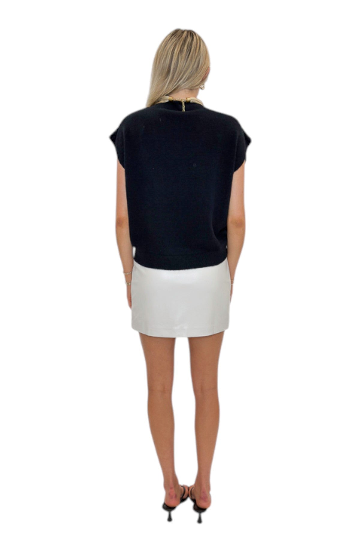 Back view of woman wearing Swagger Boutique’s Ivory Faux Leather Mini Skirt with black sweater against white studio background.