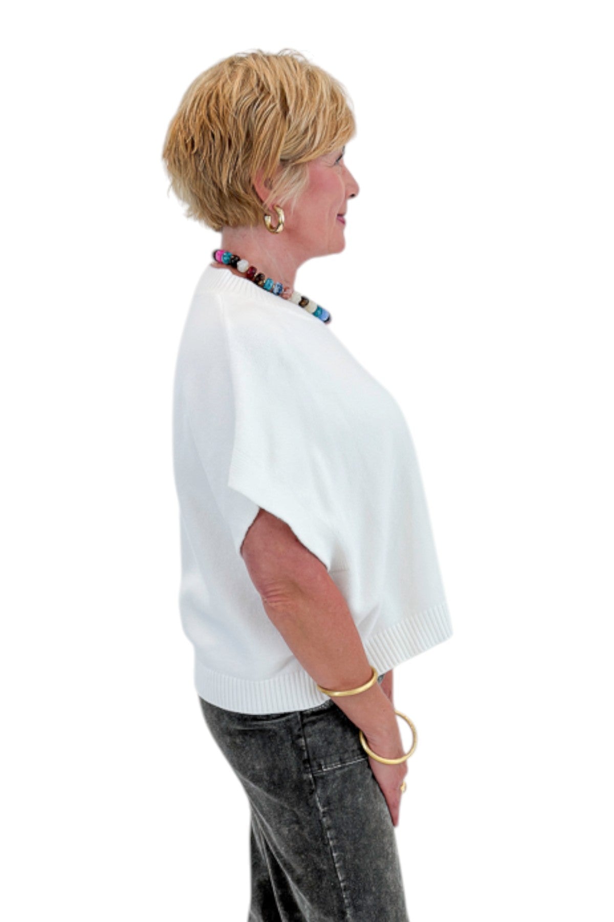 Side view of woman wearing Swagger Boutique’s Ivory Light Weight Short Sleeve Sweater with jeans against white studio background.
