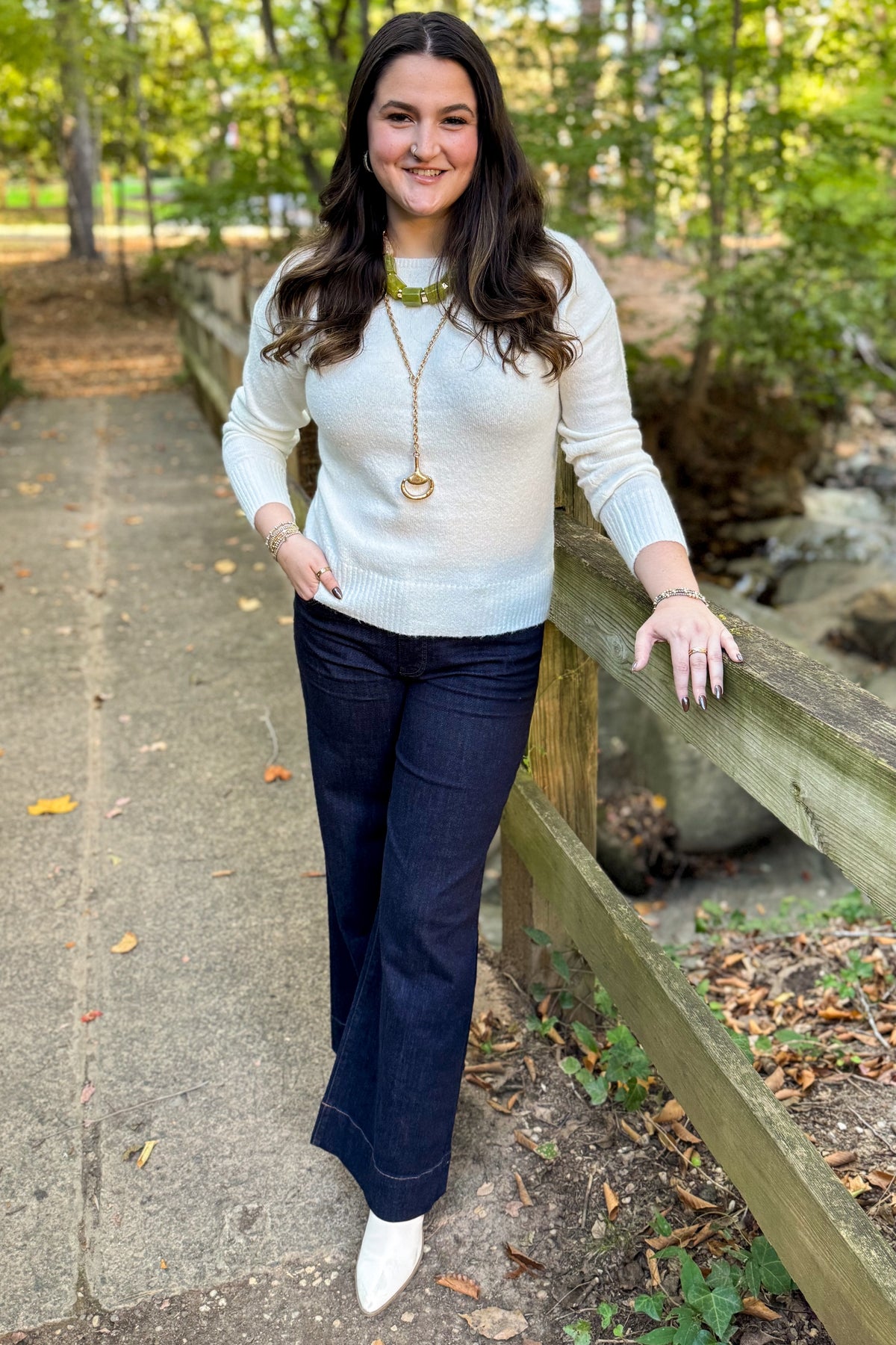 Front view of woman wearing Swagger Boutique’s Ivory Ribbed Hem Sweater with jeans standing outside on a bridge.