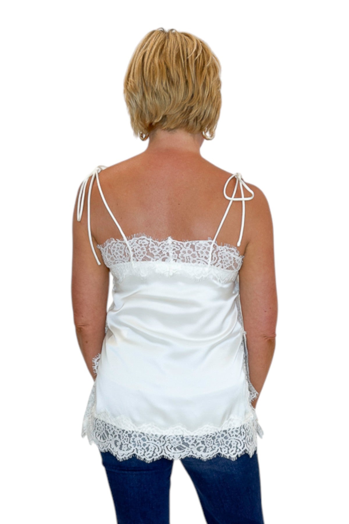 Back view of woman wearing Swagger Boutique’s Ivory Satin Lace Trim Tank Top by Entro with jeans against white studio background.