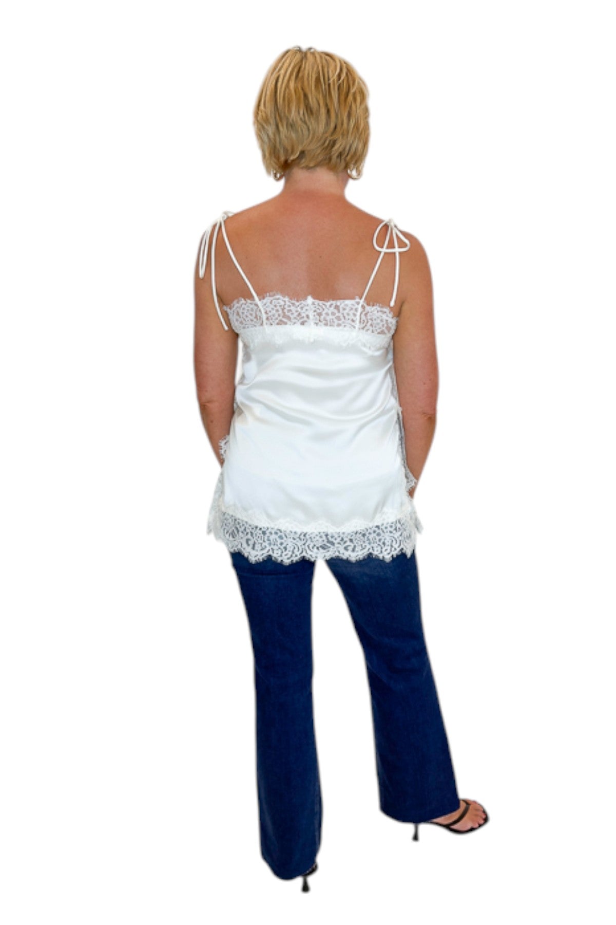 Back view of woman wearing Swagger Boutique’s Ivory Satin Lace Trim Tank Top by Entro with jeans against white studio background.