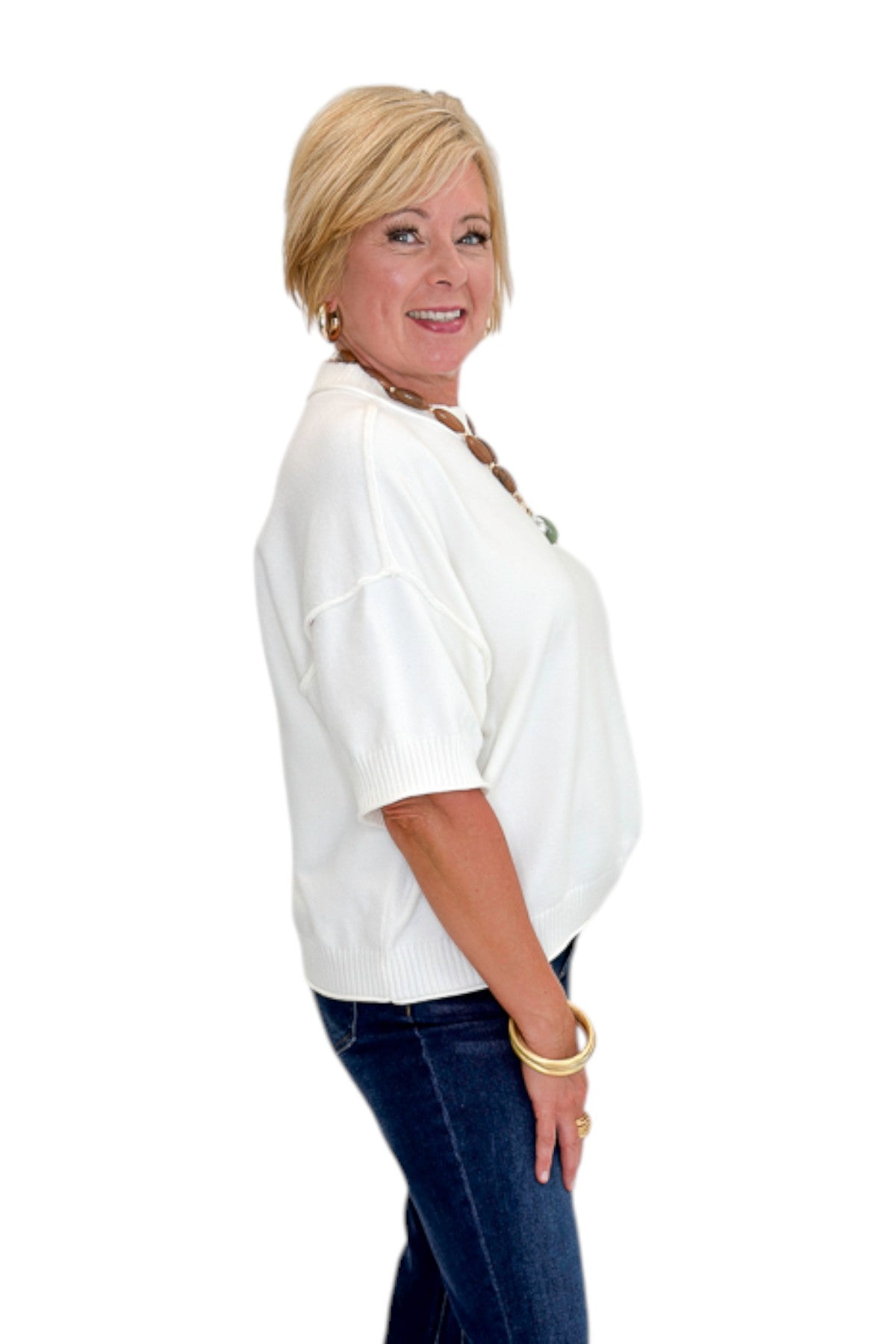 Side view of woman wearing Swagger Boutique’s Ivory Short Sleeve Sweater with jeans against white studio background.