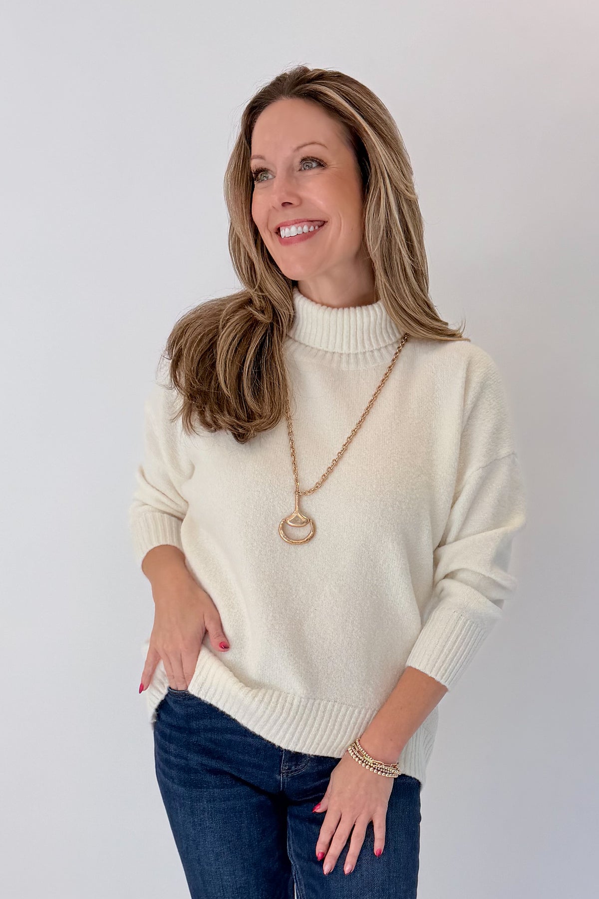 Front view of woman wearing Swagger Boutique’s Ivory Turtleneck Sweater with jeans against white studio background.
