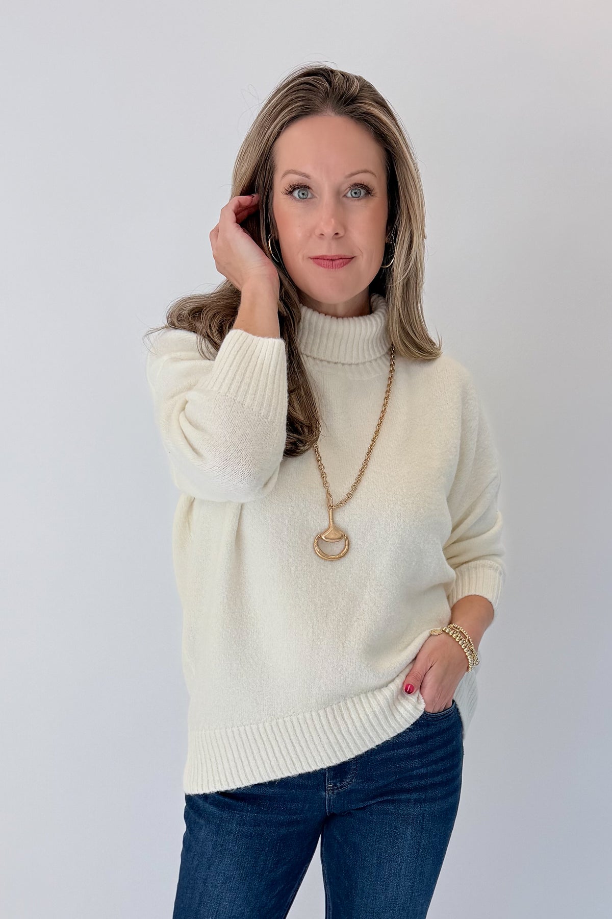 Front view of woman wearing Swagger Boutique’s Ivory Turtleneck Sweater with jeans against white studio background.
