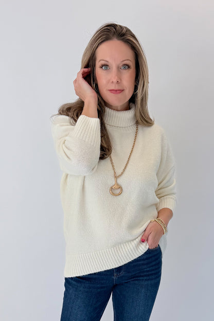 Front view of woman wearing Swagger Boutique’s Ivory Turtleneck Sweater with jeans against white studio background.
