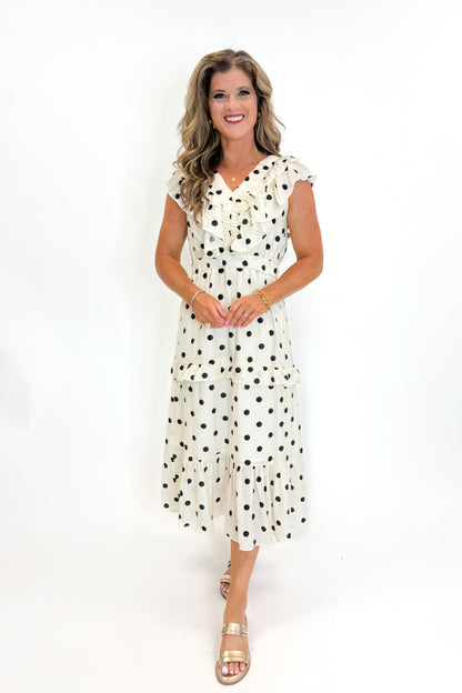 Front view of woman wearing Swagger Boutique’s Ivory &amp; Black Polka Dot Ruffle Dress with sandals against white studio background.