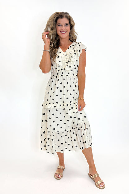 Front view of woman wearing Swagger Boutique’s Ivory &amp; Black Polka Dot Ruffle Dress with sandals against white studio background.
