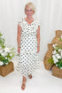 Front view of woman wearing Swagger Boutique’s Ivory & Black Polka Dot Ruffle Dress with sandals against decorative background.