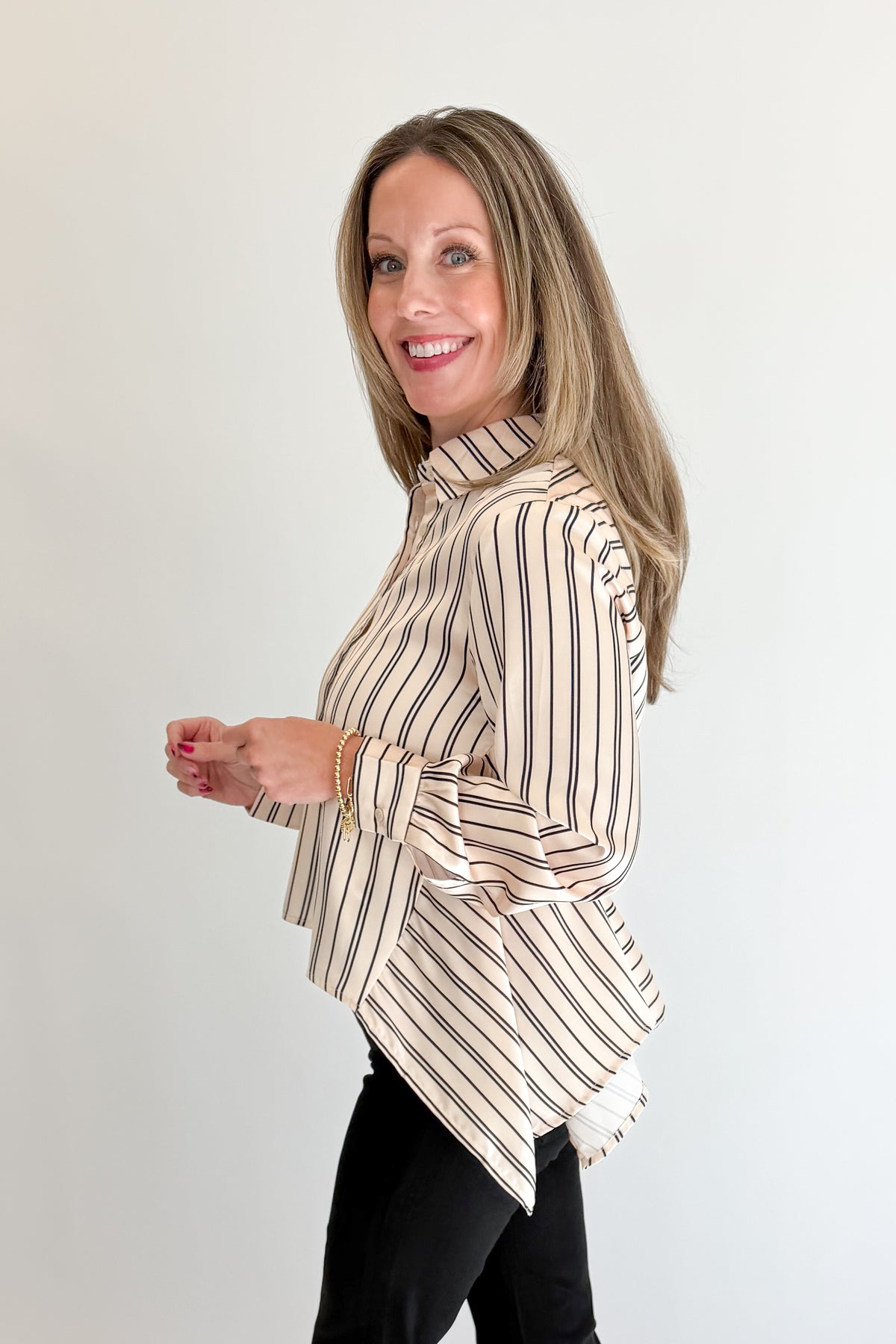 Side view of woman wearing Swagger Boutique’s Ivory &amp; Black Striped Satin Top with jeans against white studio background.