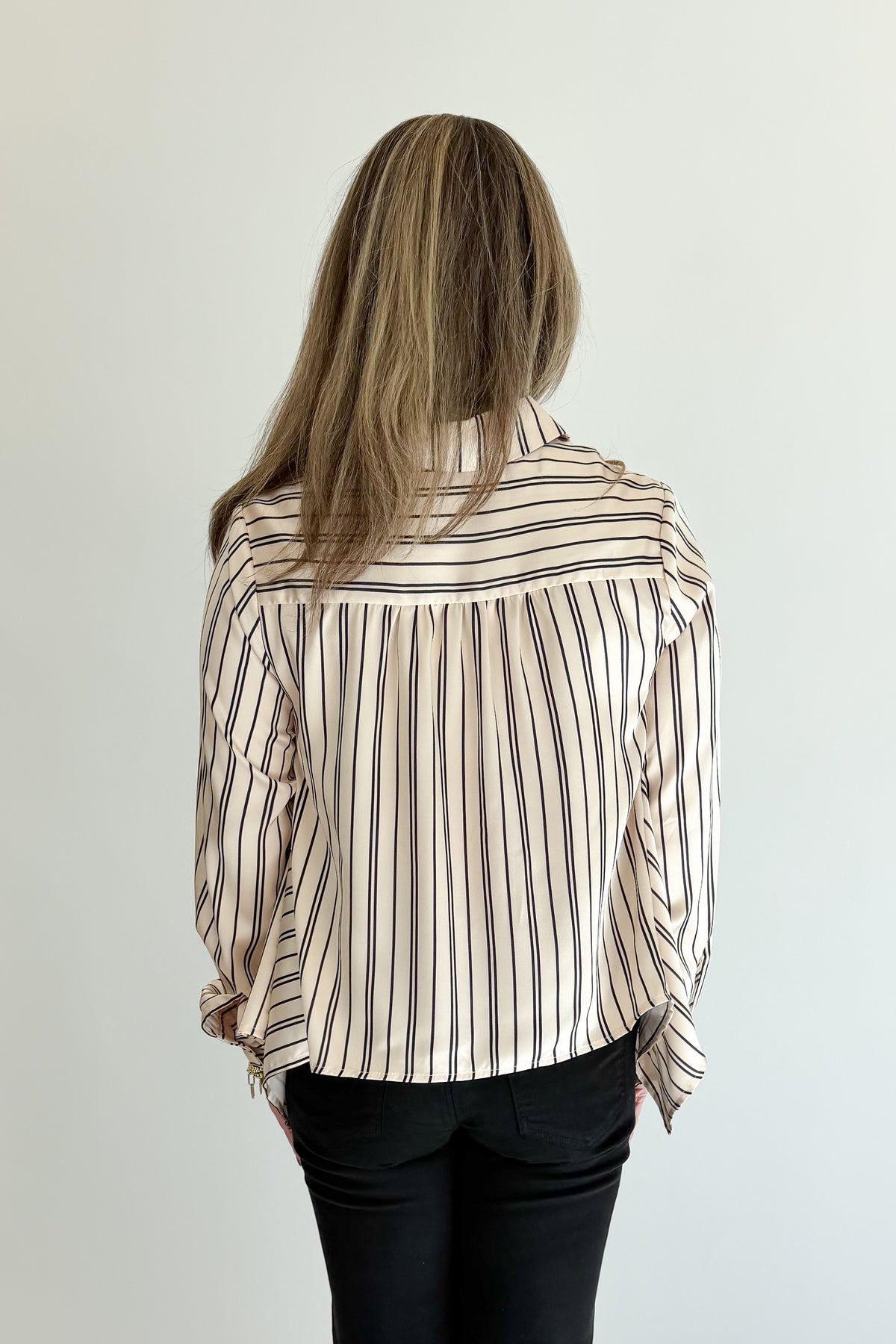 Back view of woman wearing Swagger Boutique’s Ivory &amp; Black Striped Satin Top with jeans against white studio background.